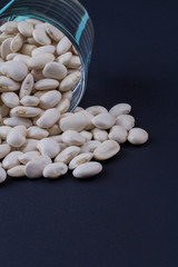 White beans spilled out from glass cup. Dark blued background.