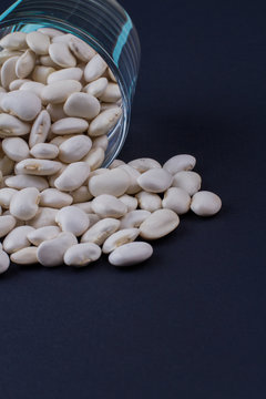 White beans spilled out from glass cup. Dark blued background.