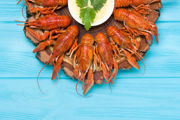 Boiled crayfish on a wooden plate with sauce on a blue background.