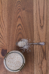 Glass jar and teaspoon with uncooked white rice. Rustic wooden background with copy space.