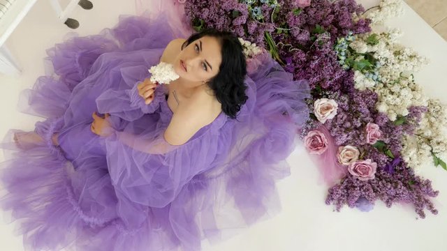 Young woman sits on the floor with lots of lilacs in the studio