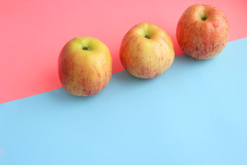 three yellow apples lie horizontally on a pink, blue background. Summer is coming, vitamins, fruits, diet, healthy sweets. Place for text, inscriptions. Beauty, design, clear lines