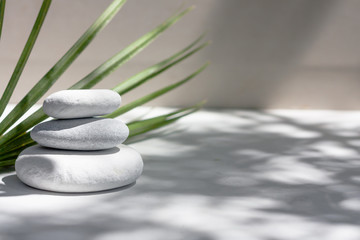 Three grey roundstones, and green leaves on white background. Spa stones, zen like concept.