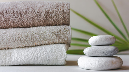 Fototapeta na wymiar Three grey roundstones and bath towels on white background with green leaves. Spa stones, zen like concept