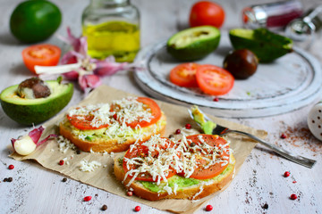 Two sandwiches with avocado, cheese and tomatoes, olive oil, garlic and spices in the background. Delicious and nutritious breakfast.