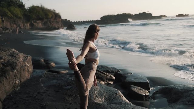 Backside view, girl doing yoga stretching, black sand volcanic beach near ocean
