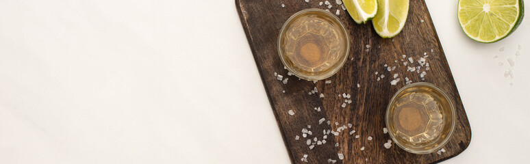 top view of golden tequila with lime, salt on wooden cutting board on white marble surface, panoramic shot