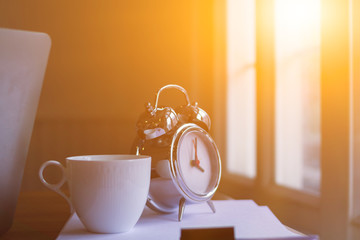 Alarm clocks and coffee mugs are placed on a wooden table by the window in the morning to prepare...