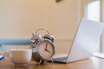 Alarm clocks and coffee mugs are placed on a wooden table by the window in the morning to prepare...