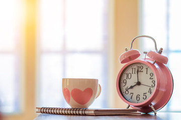 Alarm clocks and coffee mugs are placed on a wooden table by the window in the morning to prepare...