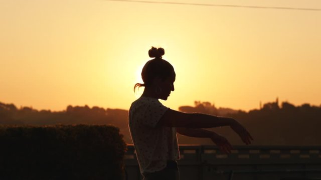 Silhouette of young woman relaxing from yoga pose at sunrise in slow motion with a strong sun backlight. The sun shines between the silhouette with a beautiful flare