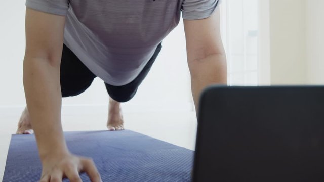 Asian man doing elbow plank up and down exercise in living room at home, watching live or video tutorial online via laptop computer. Activity during quarantine and social distance new normal concept.