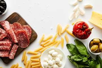 Top view of pasta, meat platter, basil leaves and ingredients on white background