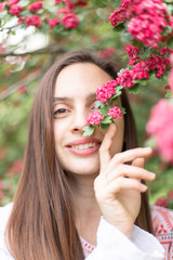 Fototapeta premium Portrait of a beautiful girl in a flowering pink tree. Flowering hawthorn tree