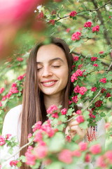 Obraz na płótnie Canvas Portrait of beautiful young smiling woman against the background of a blossoming pink flowers hawthorn tree 