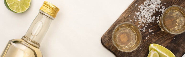 top view of golden tequila with lime, salt on wooden cutting board on white marble surface, panoramic shot