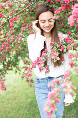 Naklejka premium Portrait of beautiful young smiling woman against the background of a blossoming pink flowers hawthorn tree 