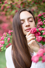Fototapeta premium Portrait of a beautiful girl in a flowering pink tree. Flowering hawthorn tree