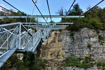Skybridge in Sochi. Suspension bridge over the gorge. Made of metal and other modern materials. The bridge and railings are trellised. There are green plants on the rock.