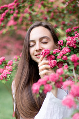 Fototapeta premium Portrait of beautiful young smiling woman against the background of a blossoming pink flowers hawthorn tree 