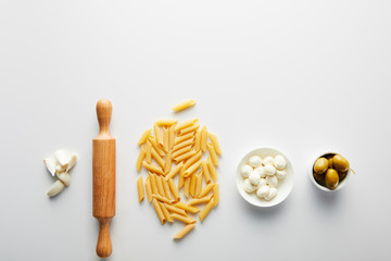 Flat lay with garlic, rolling pin, pasta and bowls with olives and mozzarella on white background