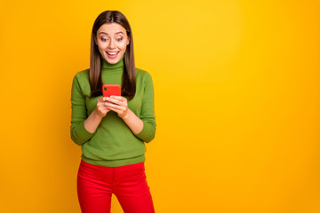 Portrait of crazy funky amazed girl using her smartphone reading social network news get like notification scream wow omg wear red pants trousers isolated over yellow color background