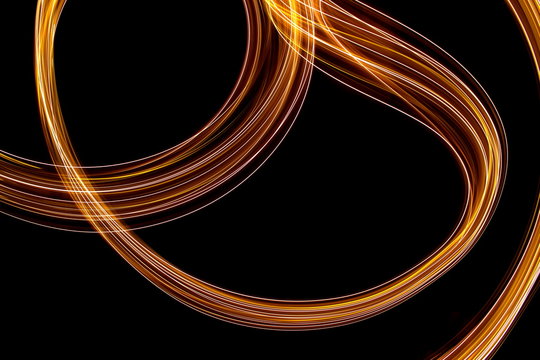 Long exposure photograph of neon gold colour in an abstract swirl, parallel lines pattern against a black background. Light painting photography.