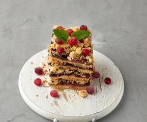 stack of square slices of baked crumble pie with blue plum on a white wooden board, delicious dessert