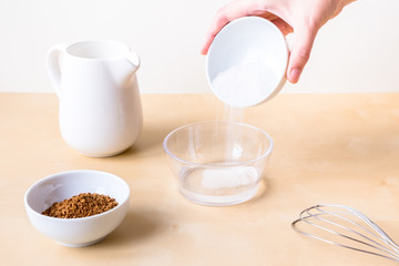 How to make dalgon coffee. Step by step photo instruction. Step 2. Add sugar to the water. Ingredients - instant coffee, sugar, water, milk and a whisk for whipping on a wooden background