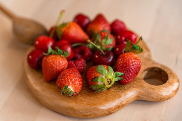 healthy and organic red spring fruit on wooden table with natural light, strawberries, cherry, raspberries, all fresh and ripe, base of a detox diet