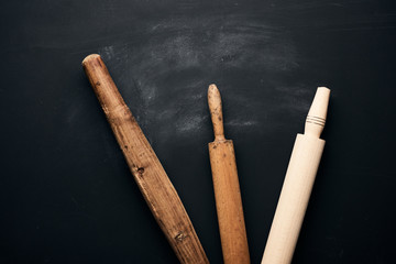 three types of wooden rolling pins for rolling dough on a black background