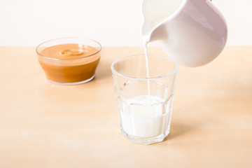 How to make coffee from dalgon. Step by step photo instruction. Step 5. Pour milk into a glass. Ingredients - instant coffee, sugar, water, milk and a whisk for whipping on a wooden background