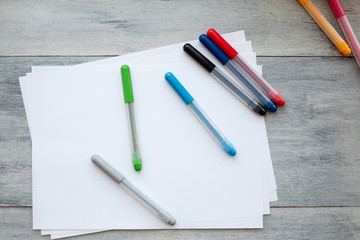 Blank A4 paper leaves and eight colored pencils are scattered on a light wooden table top view of flat objects. Home workplace by the window