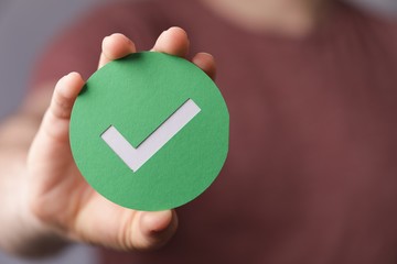 Sign of the checkmark made of paper in the hands of a man © Markus Glombitza/Wirestock