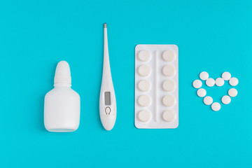 Clinical thermometer nasal spray and pills isolated on heart shaped background.