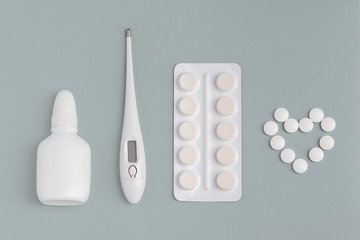 Clinical thermometer nasal spray and pills isolated on heart shaped background.