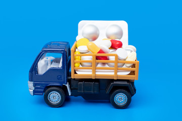 Toy truck car with pills and ampoules on a blue background. The concept of humanitarian aid, healthcare, quarantine of coronavirus, epidemic covid-19. Space for text.