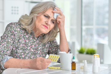 Portrait of sick senior woman with pills sitting at the table at home