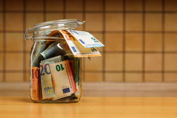 Euro banknotes in a glass jar close-up in the kitchen. The concept of economics and finance. The background is blurry.