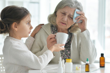 Cute girl giving medicine to sick senior woman