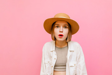 Shocked lady in hat and light summer clothes isolated on pink background, looking into camera with...