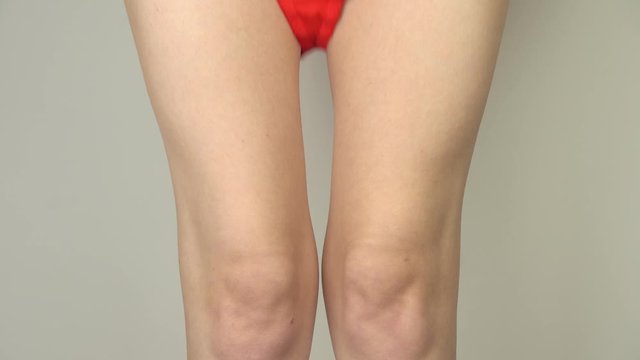 Sexy young woman dresses red panties on a gray background. Legs close up