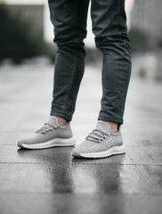 Grey sneakers on legs on the street with reflection after the rain