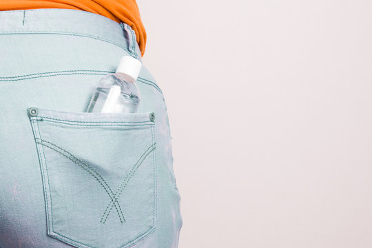 small bottle with gel sanitizer in the back pocket of bkue jeans, copy space, light backgroundwomen's jeans are put on