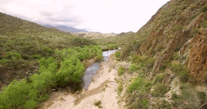 Slow low dropdown into the Aqua Fria River bed between two desert mountains, Arizona.