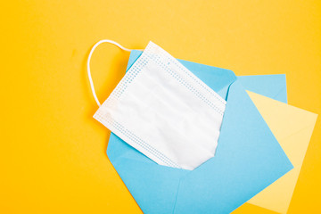 medical protective face mask in a blue gift envelope on a yellow background, a holiday during quarantine, a gift mask