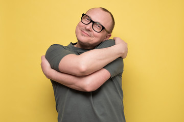 man smiling with pleasure embracing himself, keeping arms around his shoulders