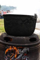 Very large cauldron cooking food during campfire, big pots on fire preparing during food festival.