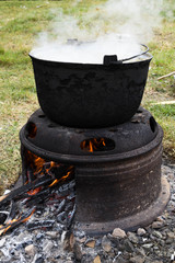 Very large cauldron cooking food during campfire, big pots on fire preparing during food festival.