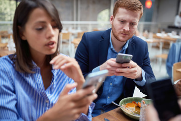 Young man and woman at business lunch texting message.